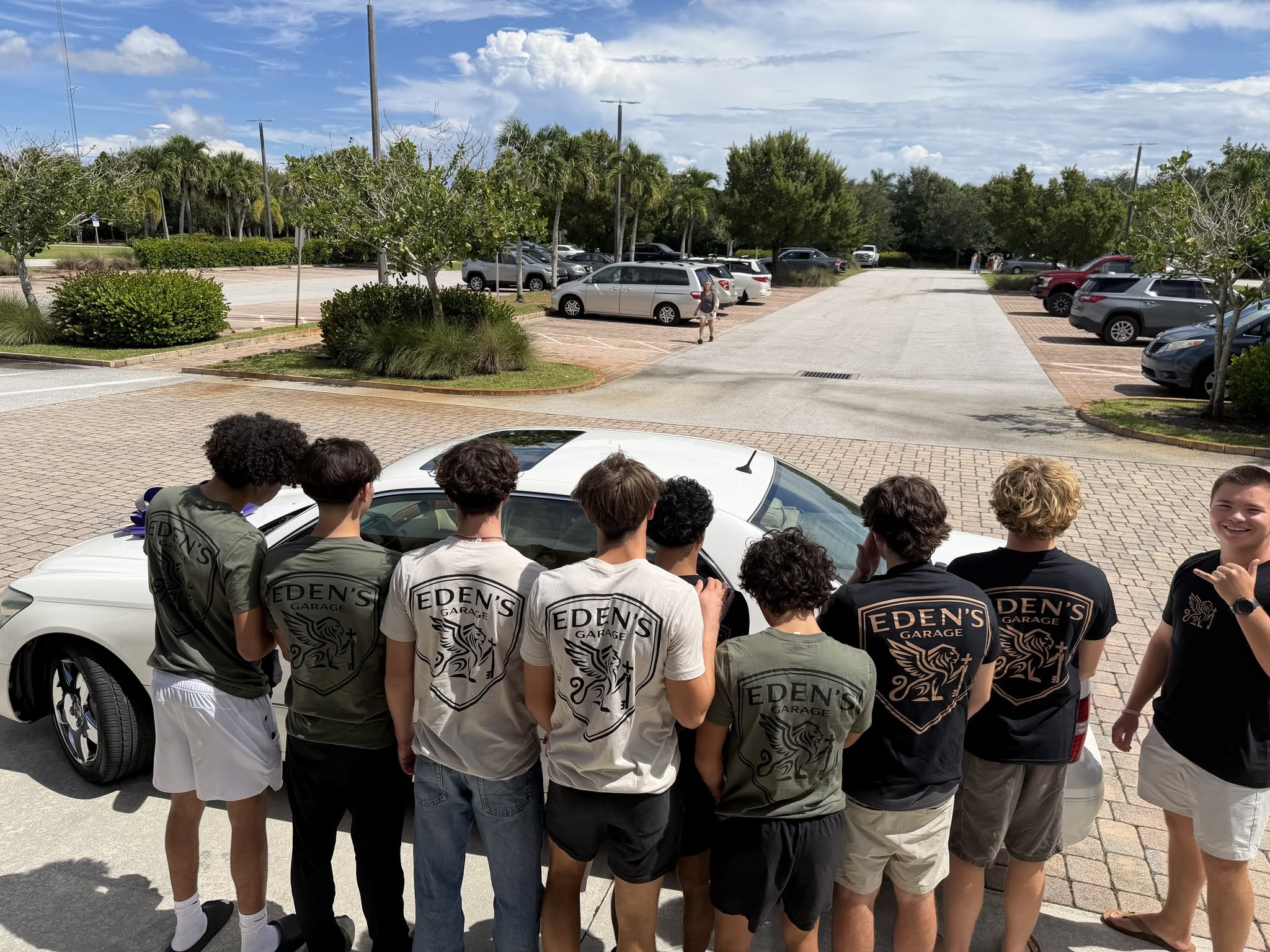 Young men in Eden's Garage T-shirts gather around a donated white car.